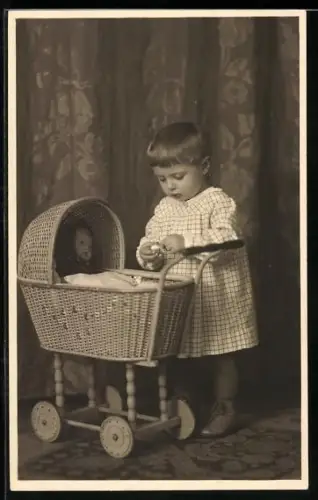 AK Kleines Kind mit einem Kinderwagen, in dem eine Puppe liegt