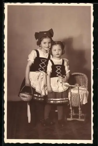 AK Zwei Kinder in Tracht neben einem Kinderwagen, in dem eine Puppe sitzt
