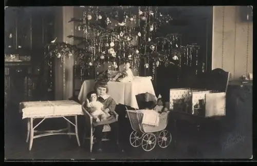 AK Junges Mädchen mit einer Puppe neben einem Kinderwagen, im Hintergrund ein Christbaum