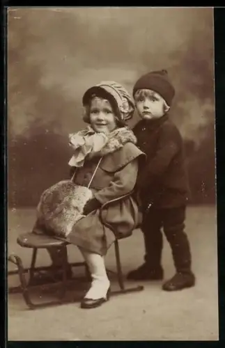 Foto-AK Kleiner Junge schiebt Mädchen auf einem Schlitten