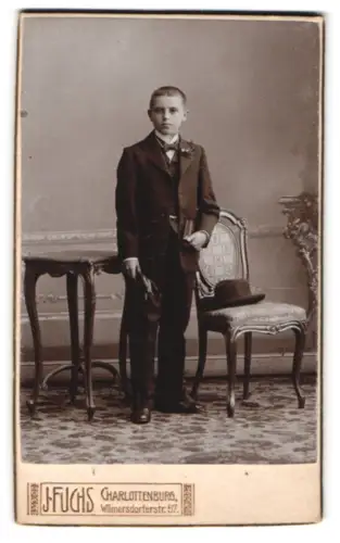 Fotografie J. Fuchs, Charlottenburg, Wilmersdorferstr. 57, Junger Mann im Anzug neben Stuhl