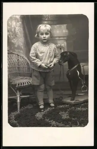 Foto-AK Kleinkind steht neben einem Schaukelpferd
