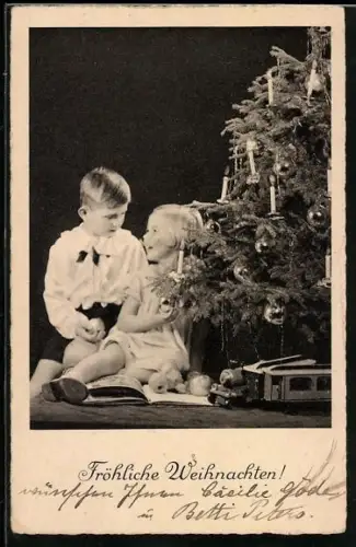 AK Zwei Kinder sitzen neben einem Weihnachtsbaum mit Spielzeugen