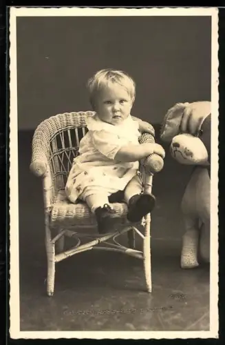 Foto-AK Kleinkind sitzt auf einem Stuhl neben einem Hunde-Plüschtier