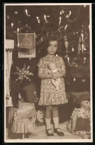 AK Kind steht an einem Weihnachtsbaum und hält eine Puppe auf dem Arm