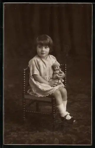 Foto-AK Kleines Kind sitzt mit einer Puppe auf dem Schoss auf einem Stuhl