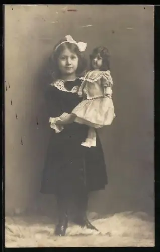 AK Mädchen mit Schleife im Haar und einer Puppe im Arm