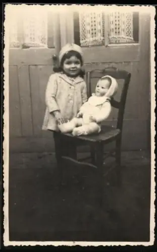 Foto-AK Kleinkind steht neben einem Stuhl, auf dem eine Puppe sitzt