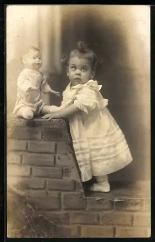 AK Kind steht auf einer Mauer, auf der eine Puppe sitzt