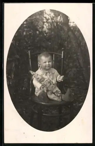 Foto-AK Kleinkind sitzt auf einem Stuhl im Garten und hat eine Puppe auf dem Schoss