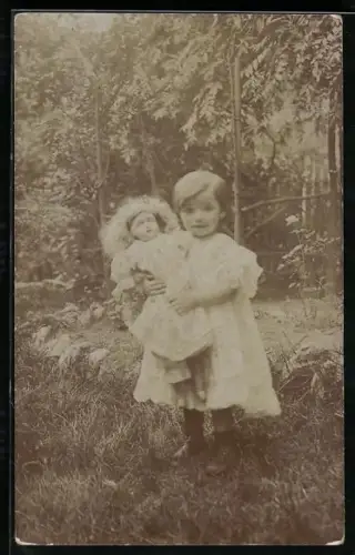 Foto-AK Kind mit einer Puppe im Arm steht im Garten
