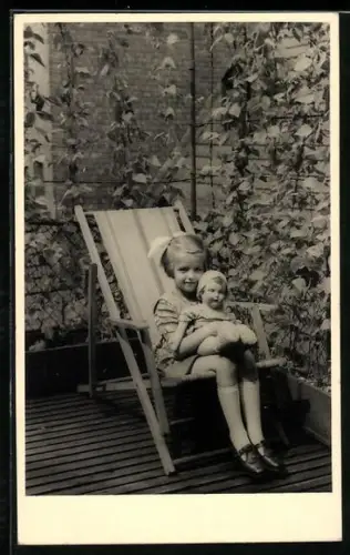 AK Kind mit Puppe auf dem Schoss sitzt in einem Gartenstuhl