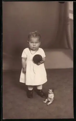 Foto-AK Kleinkind mit einem Ball in der Hand steht neben einer Babypuppe