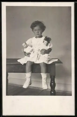 Foto-AK Kleinkind sitzt mit zwei Puppen im Arm auf einem Tisch