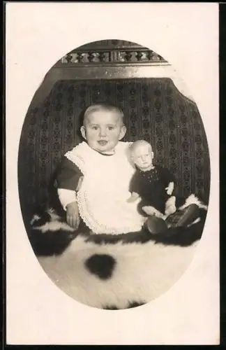 Foto-AK Kleinkind sitzt mit einer Puppe im Arm auf einem Fell