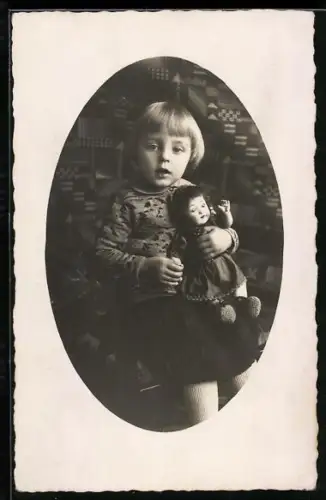Foto-AK Kleinkind vor gemusterter Tapete hält eine Puppe in den Armen