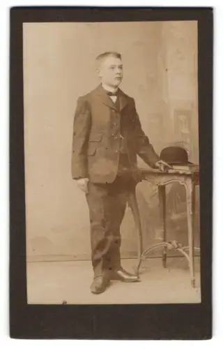 Fotografie unbekannter Fotograf und Ort, Junge im Anzug stehend neben Tisch