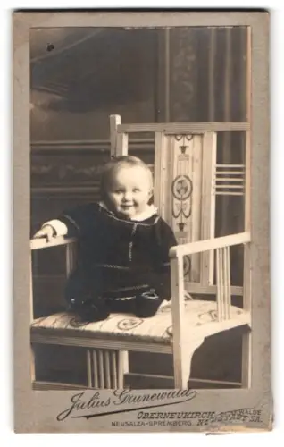 Fotografie Julius Grunewald, Oberneukirch, Lächelndes Kind auf Stuhl