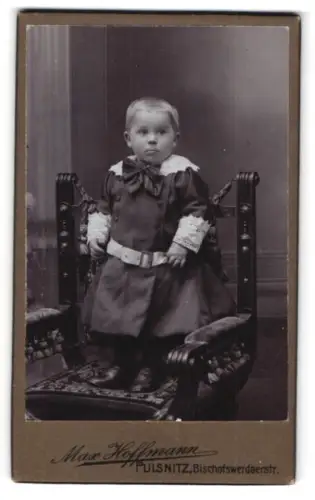 Fotografie Max Hoffmann, Pulsnitz, Bischofswerdaerstr., Kleinkind auf dekorativem Stuhl