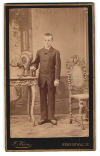 Fotografie F. Heine, Georgswalde, Stehender Junge neben Tisch