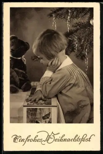 AK Kind schaut sich ein Buch an, neben ihr sitzt ein Teddy