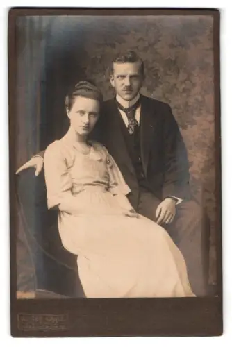 Fotografie Alfred Kahle, Pulsnitz, Paar auf Sessel vor floralem Hintergrund