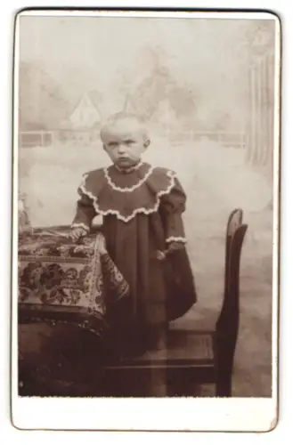 Fotografie unbekannter Fotograf und Ort, Kind im Kleid auf einem Stuhl