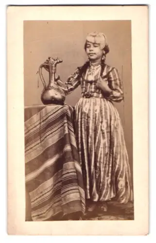Fotografie unbekannter Fotograf und Ort, Afrikanische Frau in gestreiftem Kleid mit verziertem Krug