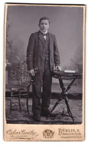 Fotografie Oskar Goetze, Berlin, Invalidenstrasse 134, Junger Mann im Anzug neben Tisch