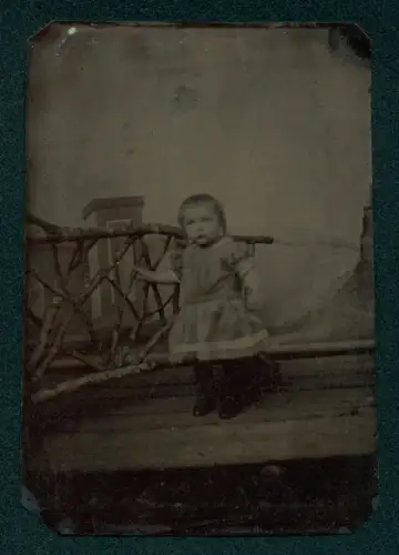 Fotografie unbekannter Fotograf und Ort, Kleinkind im Kleid vor rustikalem Geländer 1891