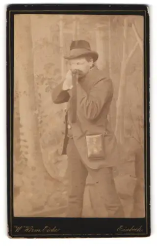 Fotografie W. Herm. Eicke, Einbeck, Neue Markt 5, Jäger mit Gewehr vor Waldkulisse, Selbstauslöser