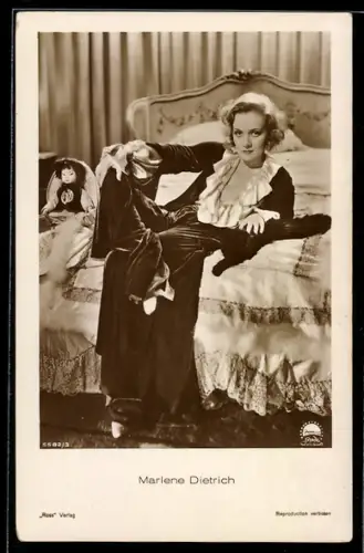 AK Schauspielerin Marlene Dietrich mit Puppe auf einem Bett