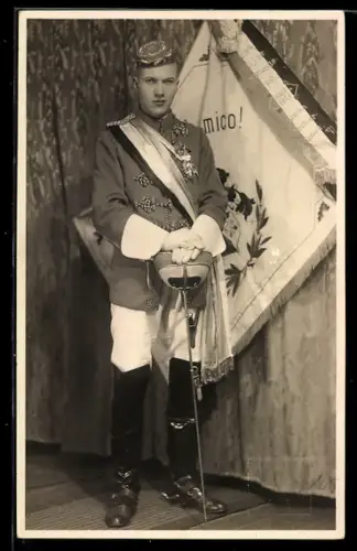 Foto-AK Student in Uniform mit Schläger und Tönnchen vor Burschenschftsfahne, studentische Szene