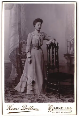 Fotografie Henri Bottiau, Bruxelles, Rue St. Josse 63, Frau neben einem dekorativen Stuhl