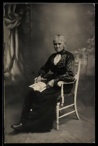Foto-AK Ältere Dame mit Buch auf Stuhl sitzend, Studiokulisse