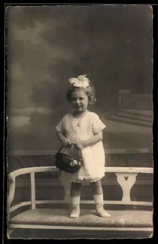 Foto-AK Kleines Mädchen mit Schleife im Haar und Korb, Studiokulisse