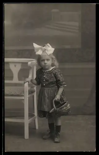 Foto-AK Kleines Mädchen mit Schleife im Haar und Korb, Studiokulisse