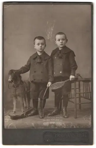 Fotografie Hermann Tietz, Hamburg, Gr. Burstah 12/14, Zwei Jungen mit Spielzeugpferd und Tennisschläger