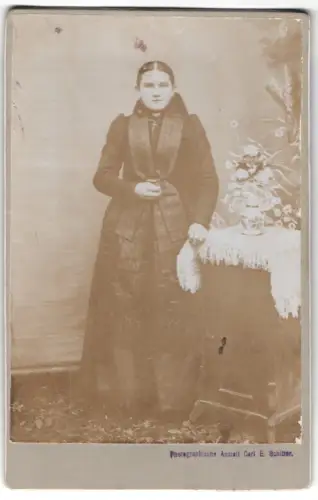 Fotografie Carl E. Schitter, Ort unbekannt, Frau in Tracht neben einem Tisch mit Blumenarrangement