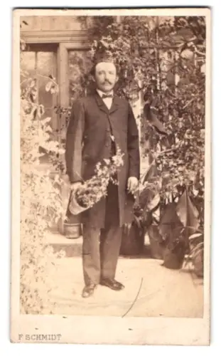 Fotografie F. Schmidt, Hamburg, Neustädter Fuhlentwiete 35, Herr im Anzug im Garten mit Blumentopf