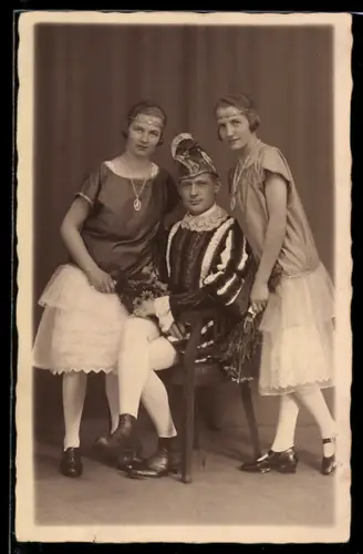 Foto-AK Sitzender Narr mit zwei hübschen Frauen