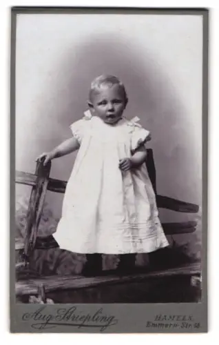 Fotografie Aug. Striepling, Hameln, Emmern Str. 18, Kleinkind in weissem Kleid auf Holzbank