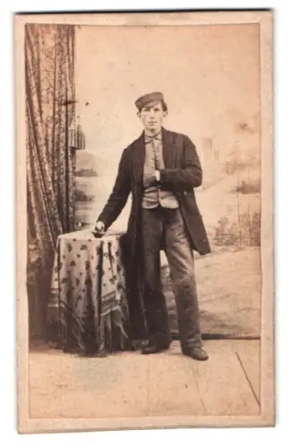 Fotografie unbekannter Fotograf und Ort, Junger Mann stehend neben Tisch