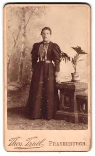 Fotografie Thos. Trail, Fraserburgh, Frau neben Tisch mit Pflanze