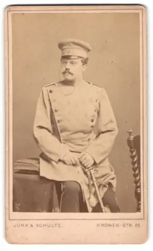 Fotografie Junk & Schultz, Berlin, Kronen-Strasse 25, Offizier im Überrock mit Schirmmütze und Säbel