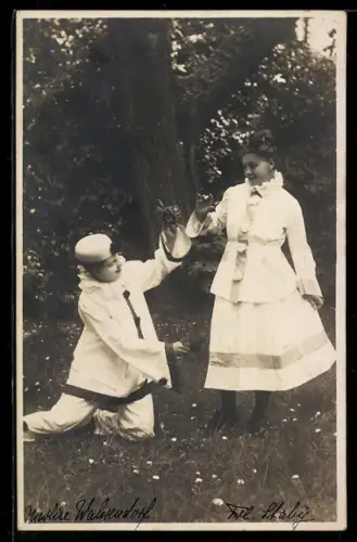 Foto-AK Harlekin kniet vor einer Dame auf einer Wiese