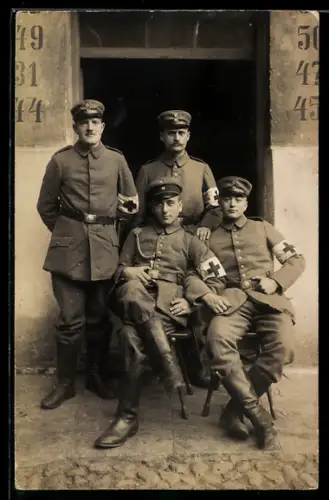 Foto-AK Vier Soldaten mit Armbinden Rotes Kreuz vor einem Gebäudeeingang