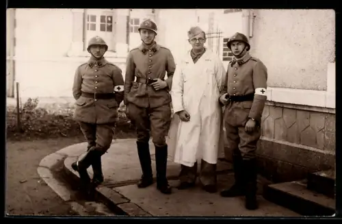 Foto-AK Sanitätssoldaten mit Rotkreuz-Armbinden, Soldat im weissen Kittel vor einer Gebäudewand