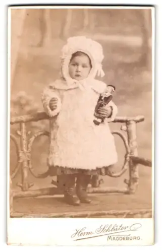 Fotografie Herm. Schlüter, Magdeburg, Ecke Breiteweg, Kleines Kind in Winterkleidung mit Puppe