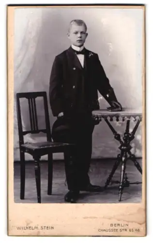 Fotografie Wilhelm Stein, Berlin, Chausseestr. 65/66, Junge in Anzug mit Tisch und Stuhl